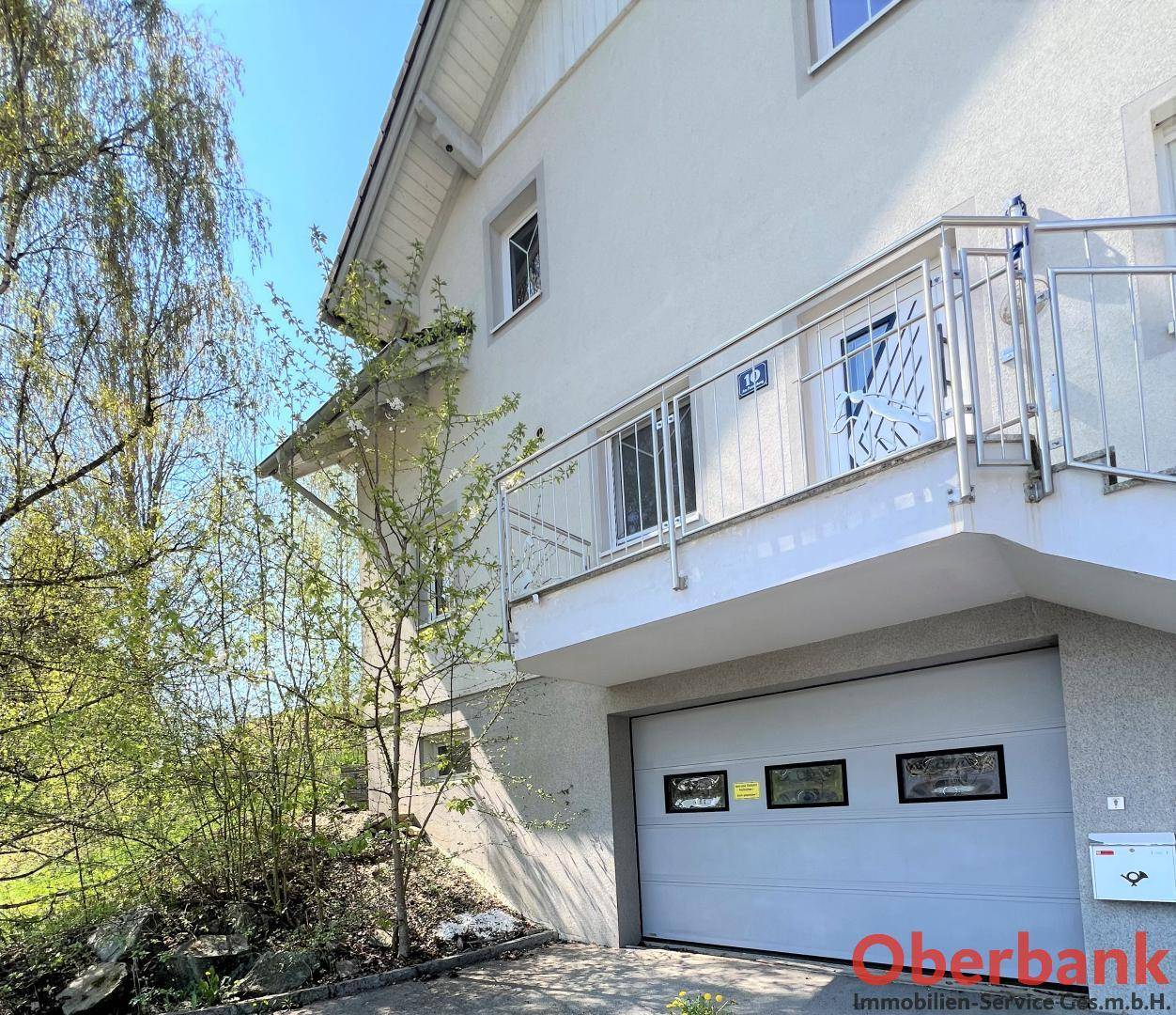 Seitenansicht des Hauses mit integrierter Garage und einer Außentreppe, die zum oberen Eingangsbereich führt.