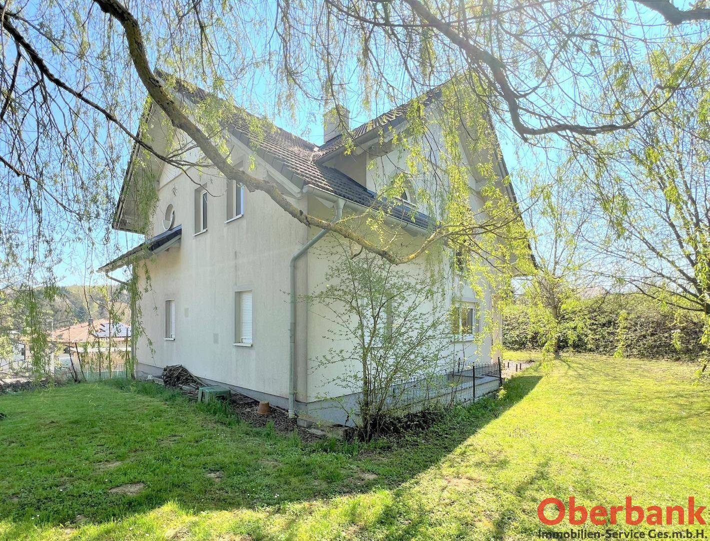 Rückansicht des Hauses mit grüner Umgebung und Bäumen unter blauem Himmel.