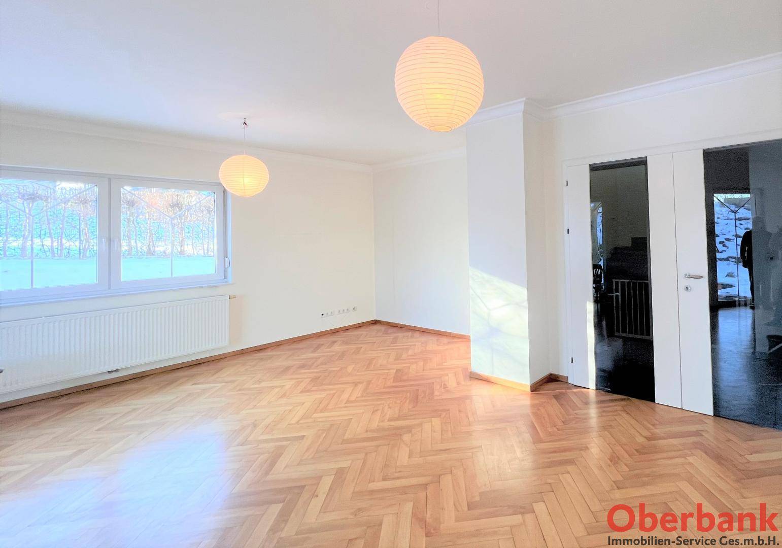 Heller Wohnbereich mit Parkettboden, großen Fenstern und viel Tageslicht.