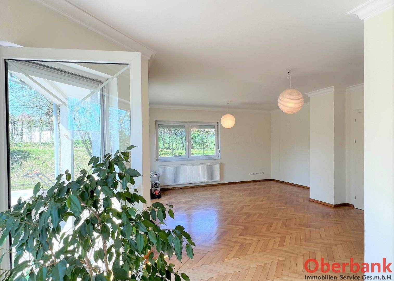 Geräumiges Wohnzimmer mit Parkettboden und Blick ins Grüne durch große Fenster.