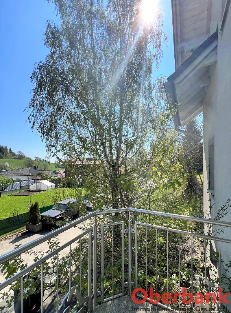 Blick von einem Balkon mit Edelstahlgeländer auf die Straße und die umliegende grüne Landschaft.