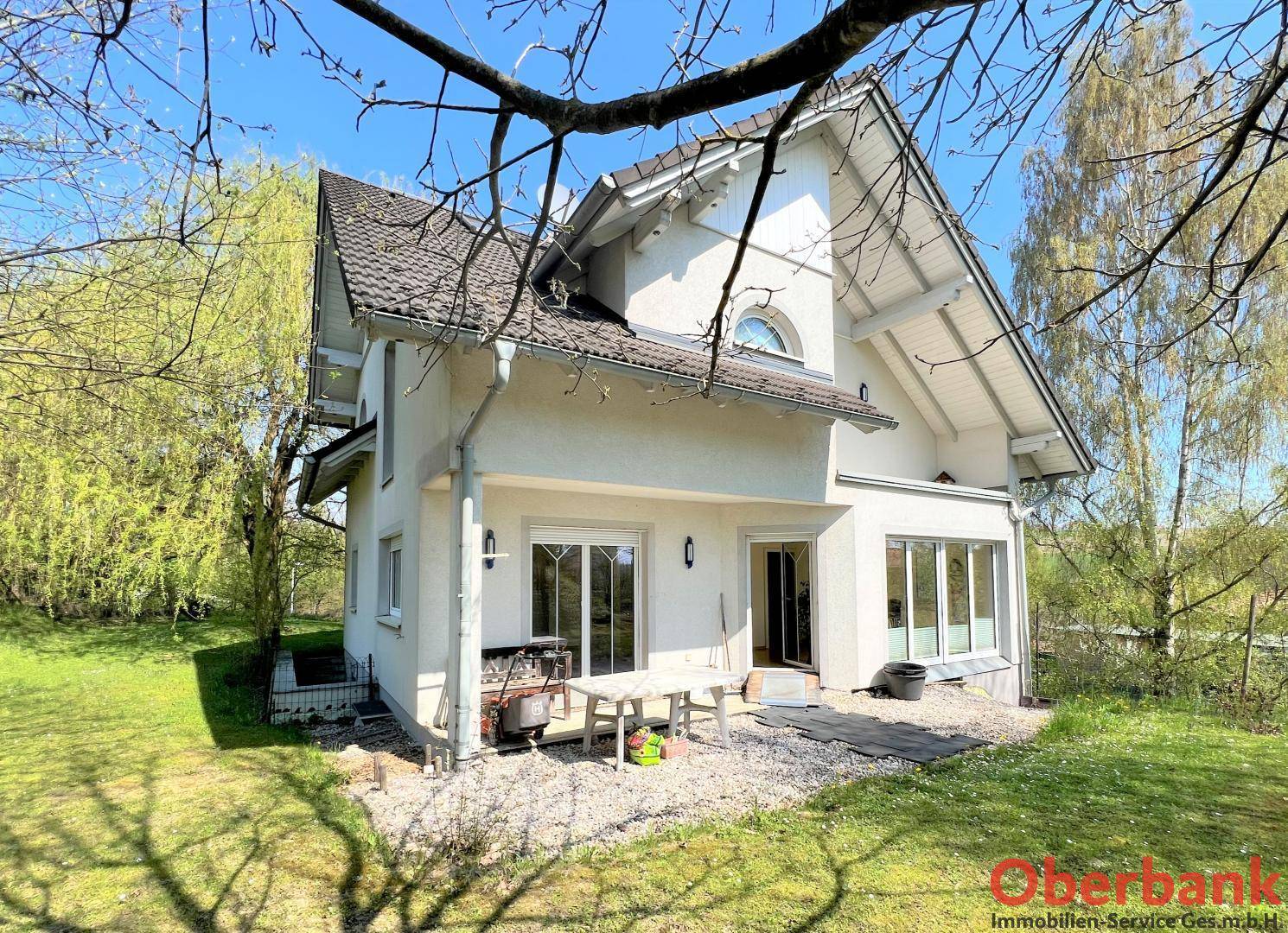 Rückseite des Hauses mit einer kleinen gepflasterten Terrasse, Gartenmöbeln und Zugang zum grünen Garten.