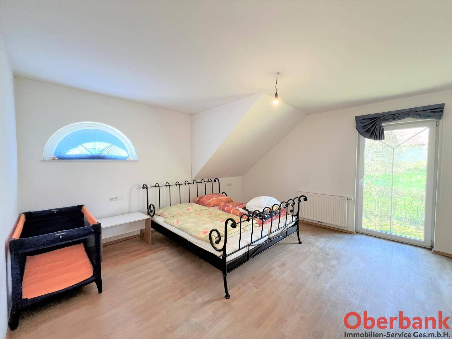 Schlafzimmer im Dachgeschoss mit Holzboden, schmiedeeisernem Bett und Zugang zum Balkon.