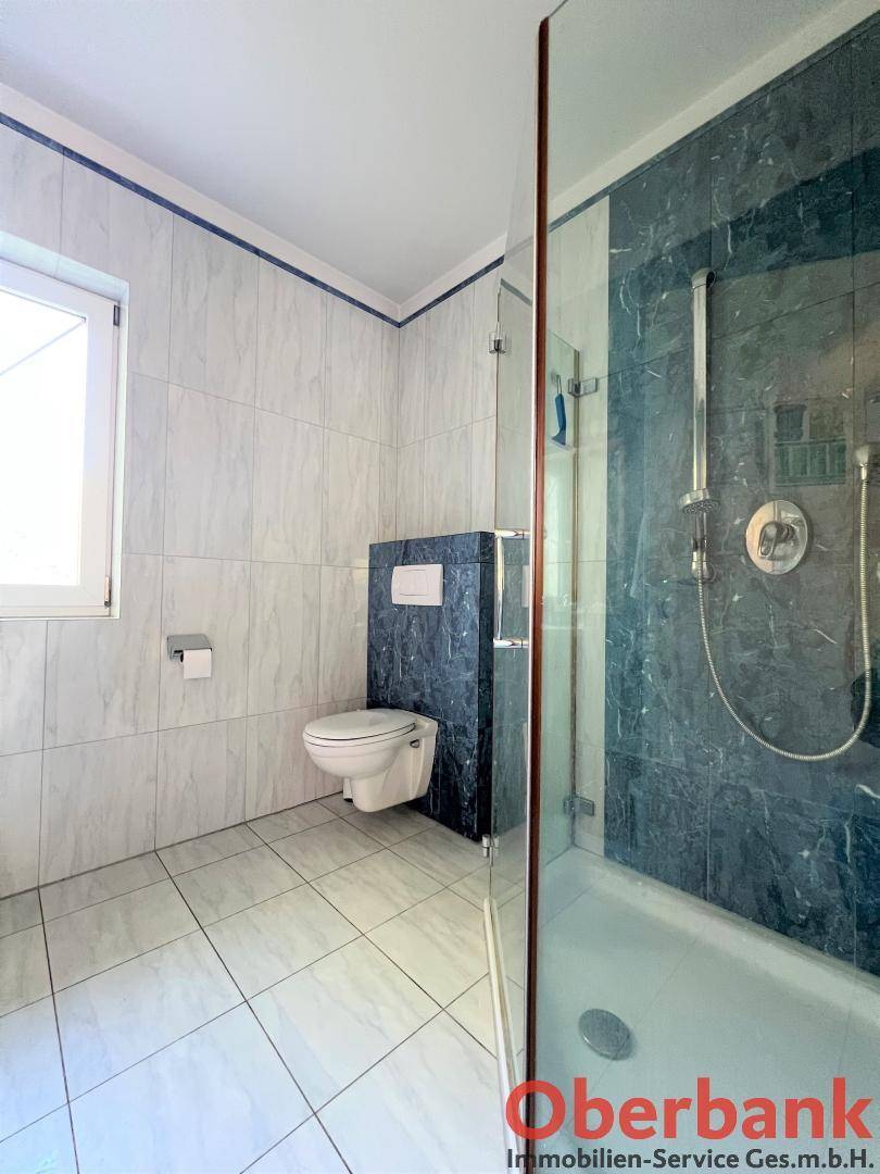 Badezimmer mit Duschkabine, Wand-WC und blauen Akzentfliesen.