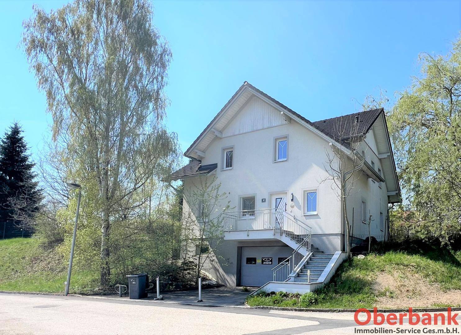 Vorderansicht des Hauses mit Eingangsbereich, Treppe und integrierter Garage im Untergeschoss.