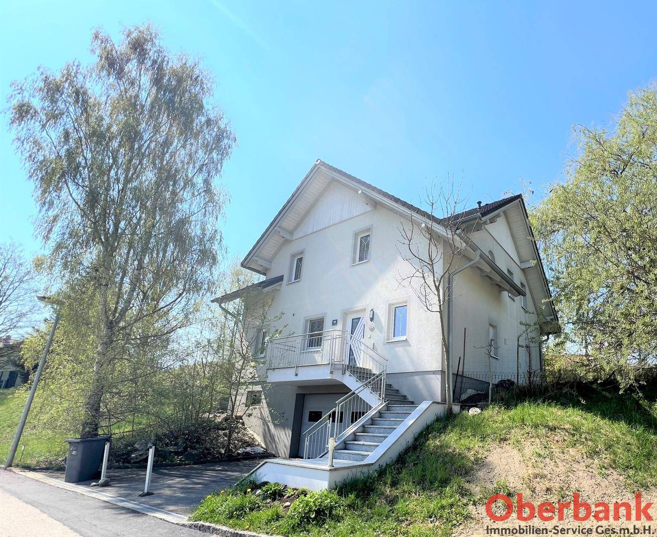 Ansicht des Hauses auf einem Hanggrundstück mit Außentreppe, Garage und umgebender Grünfläche.