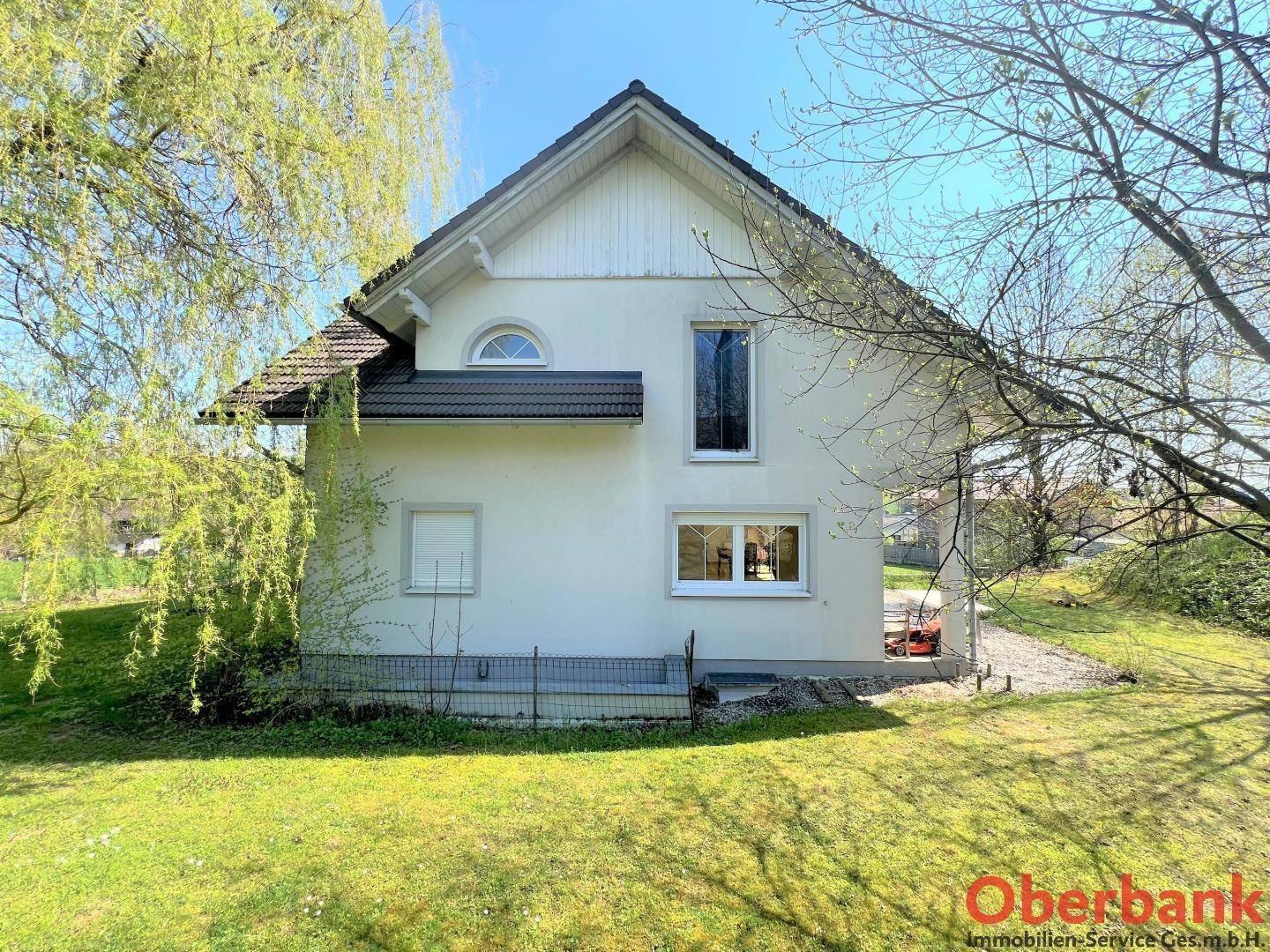Seitenansicht des weißen Einfamilienhauses mit Satteldach und mehreren Fenstern, umgeben von Grünflächen.