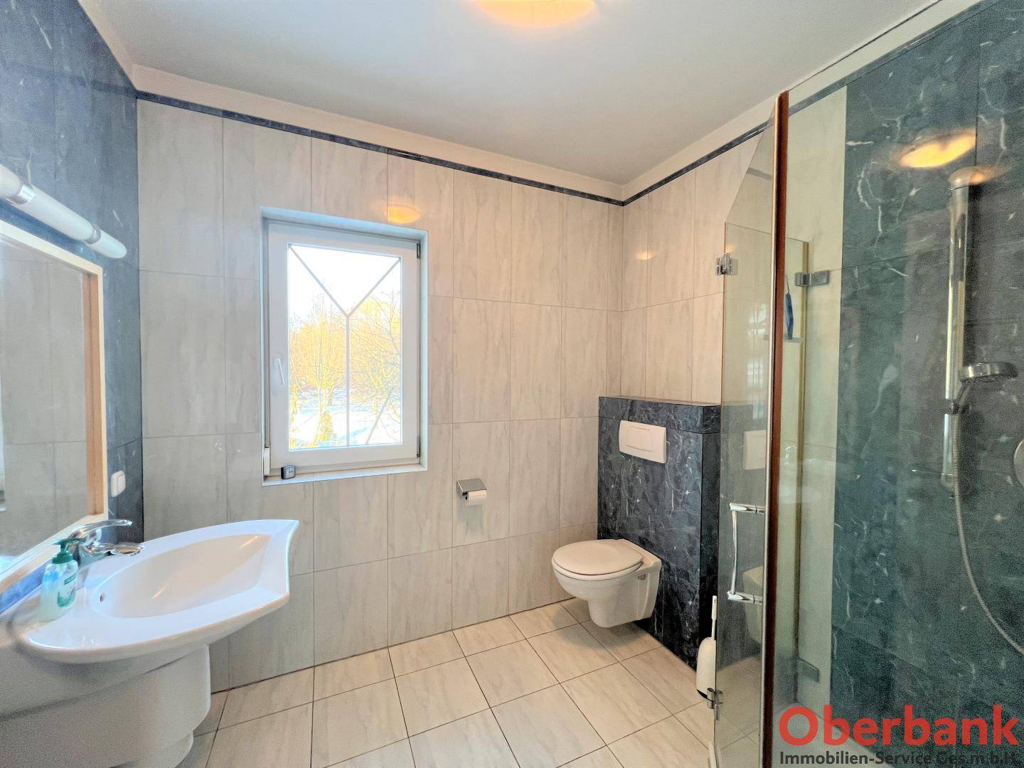 Modernes Badezimmer mit blauen und weißen Fliesen, Dusche und Fenster.