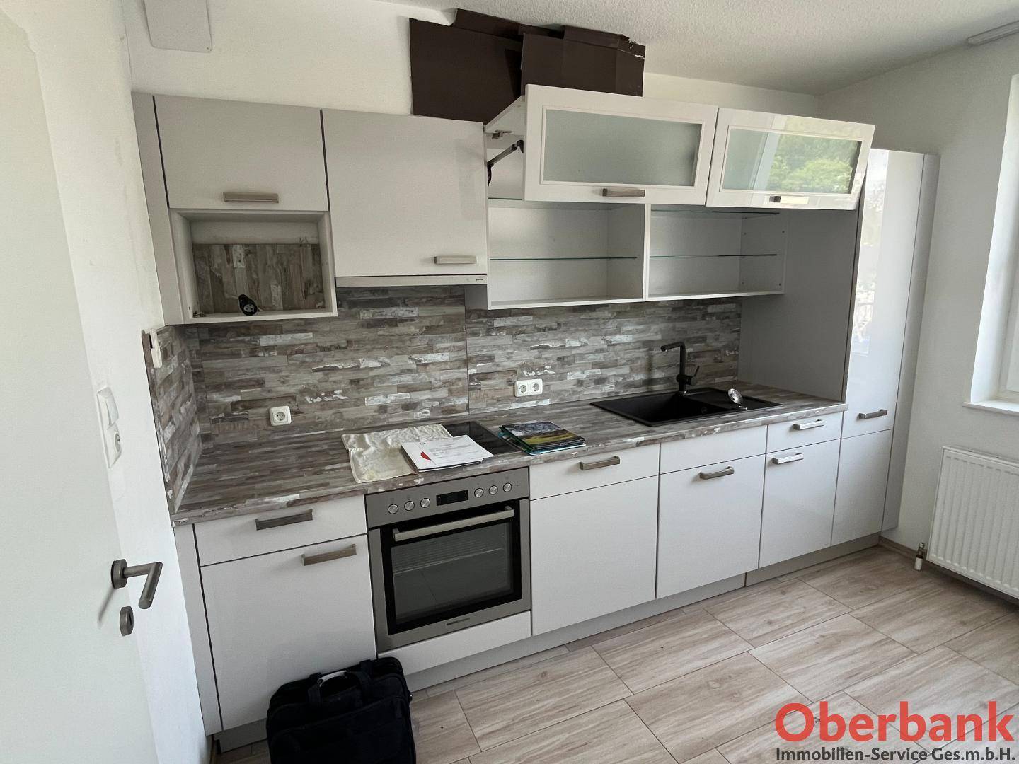 Moderne Küche mit weißen Hochglanzschränken, integriertem Backofen und gemusterter Rückwand.
