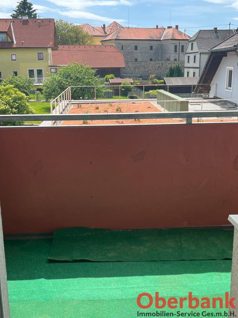 Balkon mit roter Brüstung und Blick auf die umliegenden Häuser und den blauen Himmel.