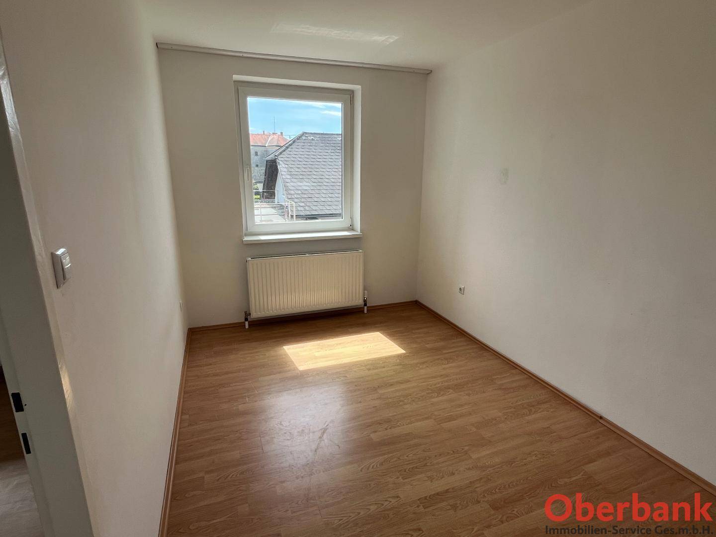 Kleines Zimmer mit Laminatboden und einem Fenster, das den Raum mit Tageslicht erhellt.