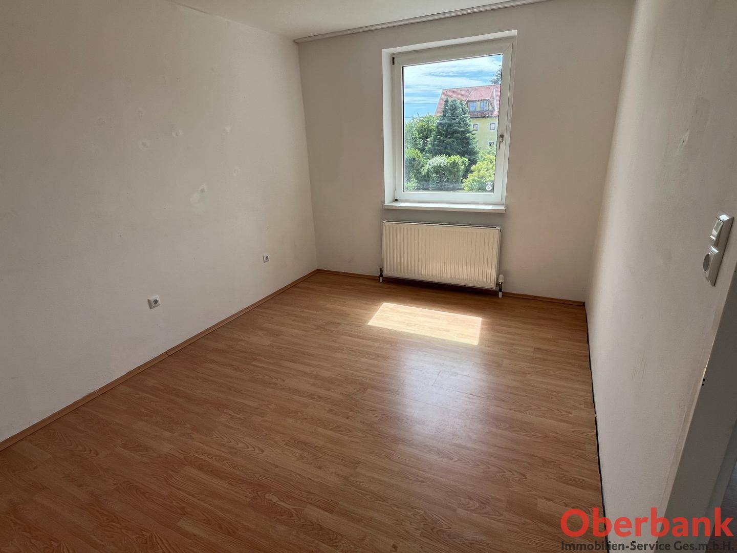 Helles Zimmer mit Laminatboden und einem Fenster, das viel Tageslicht hereinlässt.