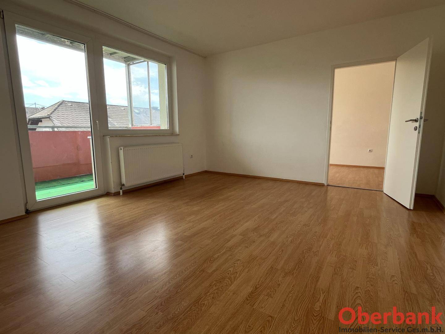 Geräumiges Wohnzimmer mit Laminatboden und großen Fenstern, die Zugang zu einem Außenbereich bieten.