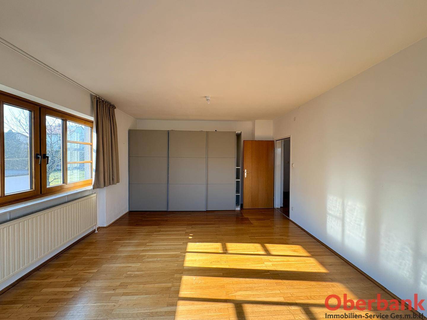 Geräumiges Schlafzimmer mit Holzboden, Fenster und praktischen Einbauschränken.
