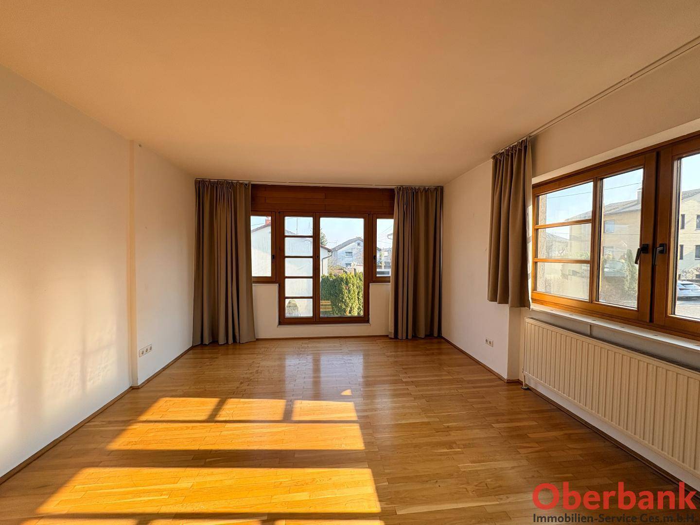 Heller Raum mit Holzboden und mehreren Fenstern, die viel Tageslicht hereinlassen.