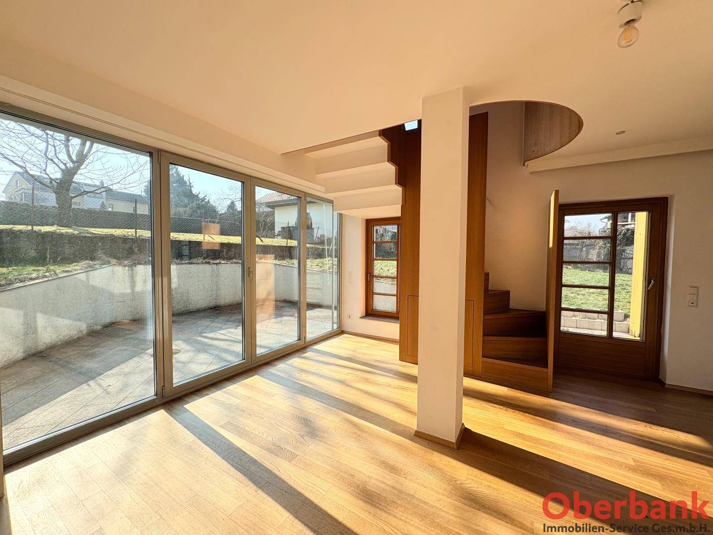 Lichtdurchfluteter Wohnbereich mit Holztreppe, großen Fenstern und Zugang zur Terrasse.