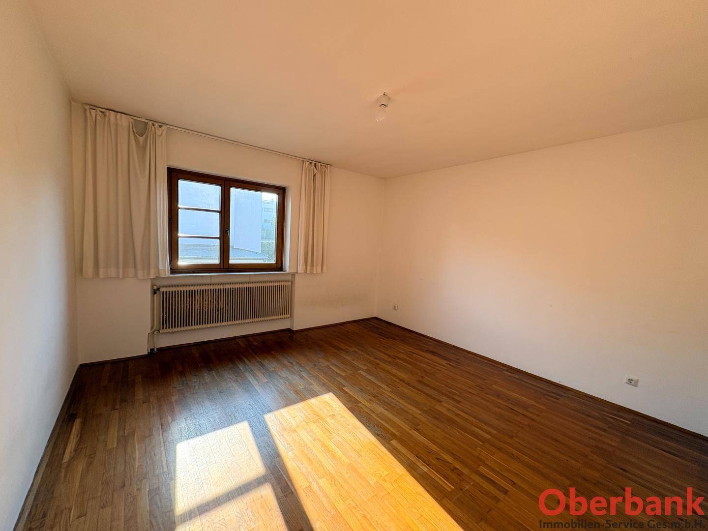 Gemütliches Schlafzimmer mit Holzboden, Fenster und Heizkörper, bereit für persönliche Einrichtung.