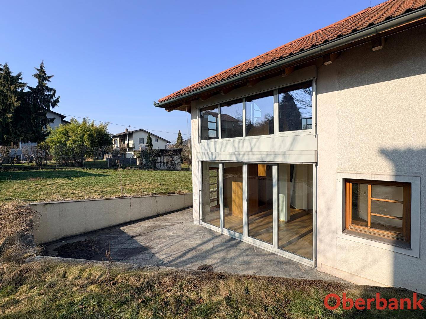 Seitliche Ansicht des Hauses mit großer Terrasse und bodentiefen Fenstern, umgeben von Grünflächen.