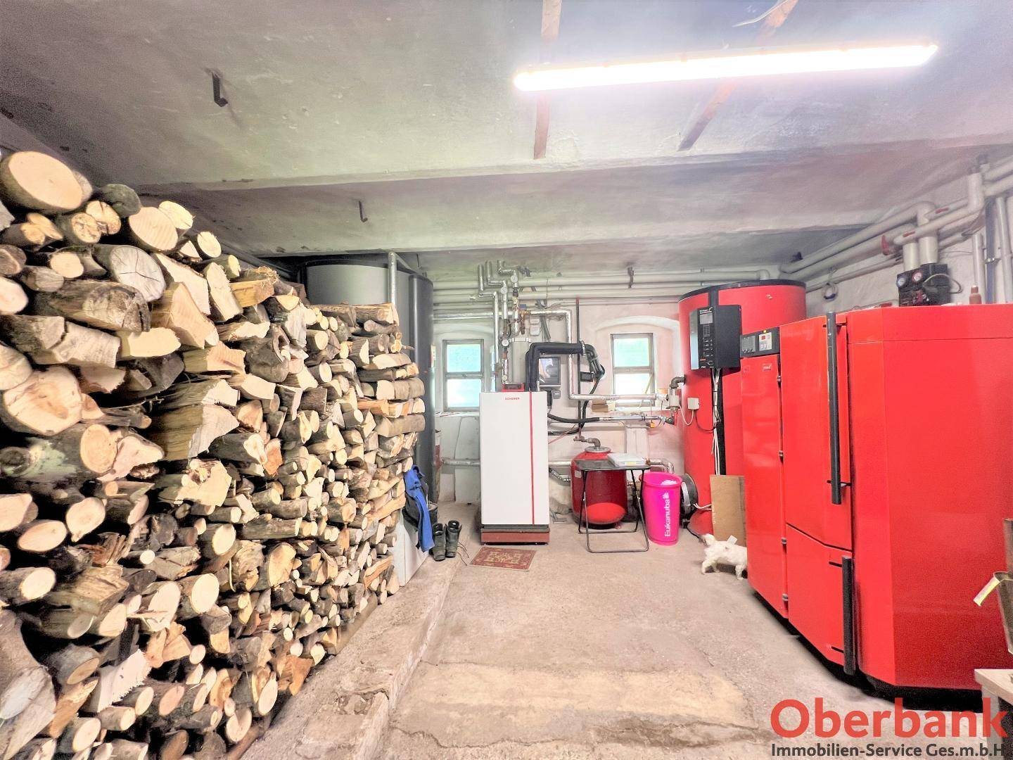 Heizungsraum mit zwei großen roten Heizkesseln und einem Vorrat an Brennholz für die Anlage.