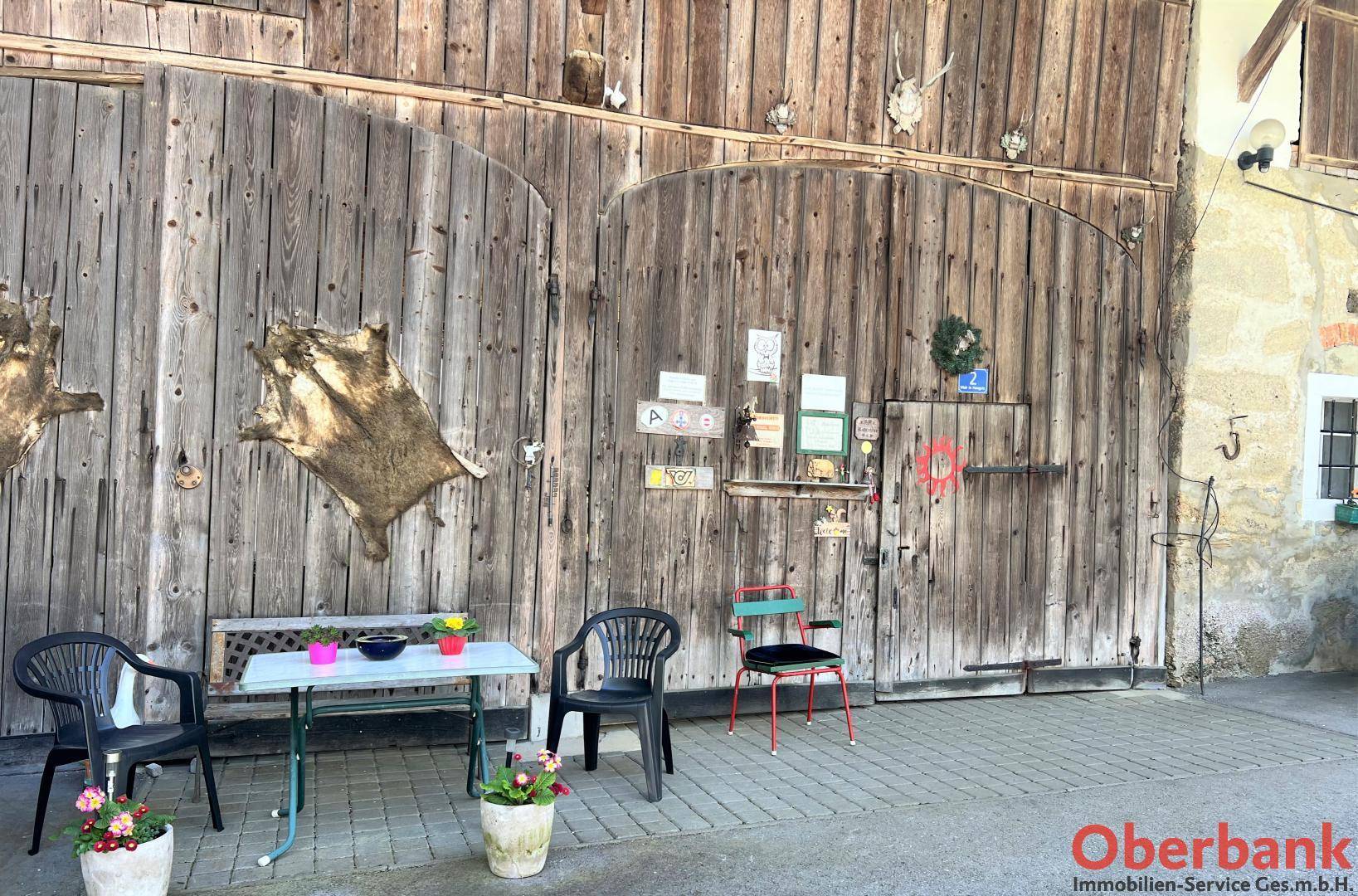 Rustikale Holzscheunentore mit Jagdtrophäen und einem kleinen, einfachen Sitzbereich davor auf gepflastertem Boden.