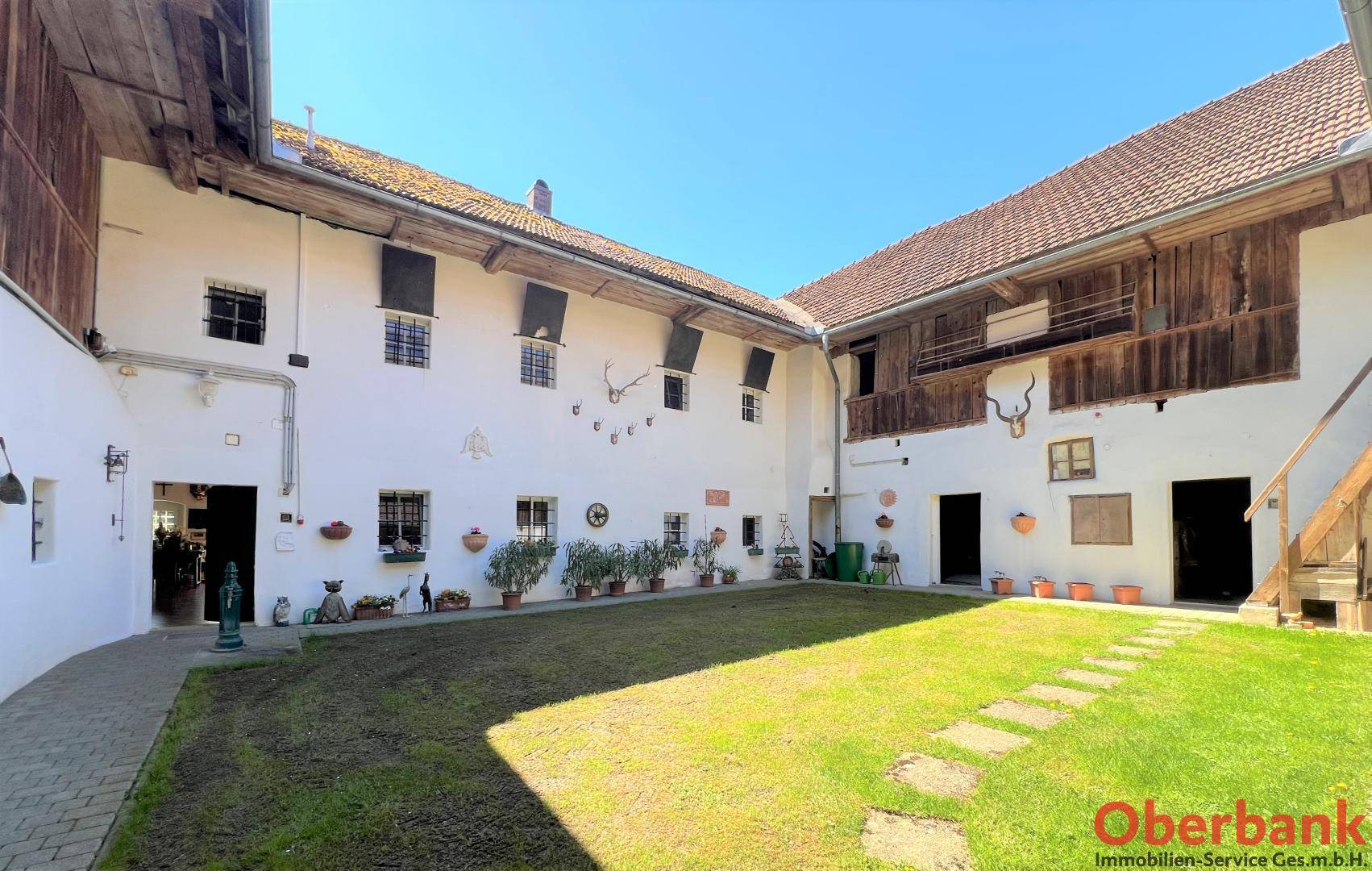 Idyllischer Innenhof eines Bauernhauses mit Rasenfläche, weiß getünchten Wänden und Holzelementen.