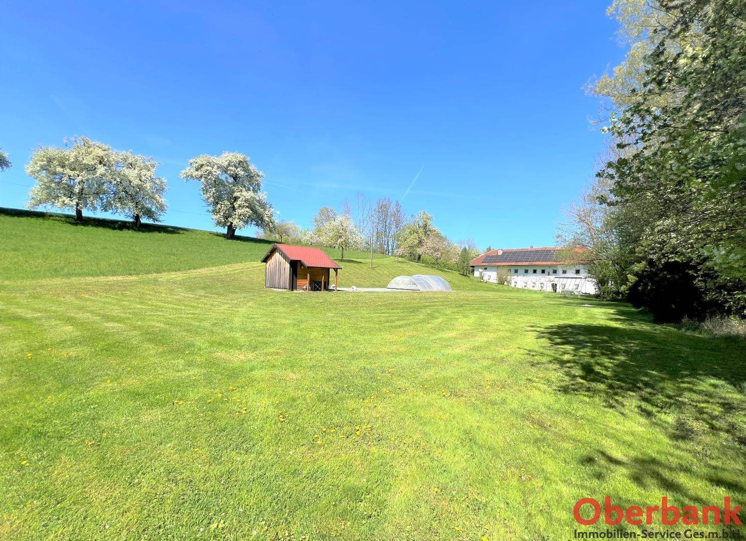 Weitläufige grüne Hügellandschaft mit einem kleinen Holzhaus und dem Bauernhaus in der Ferne.