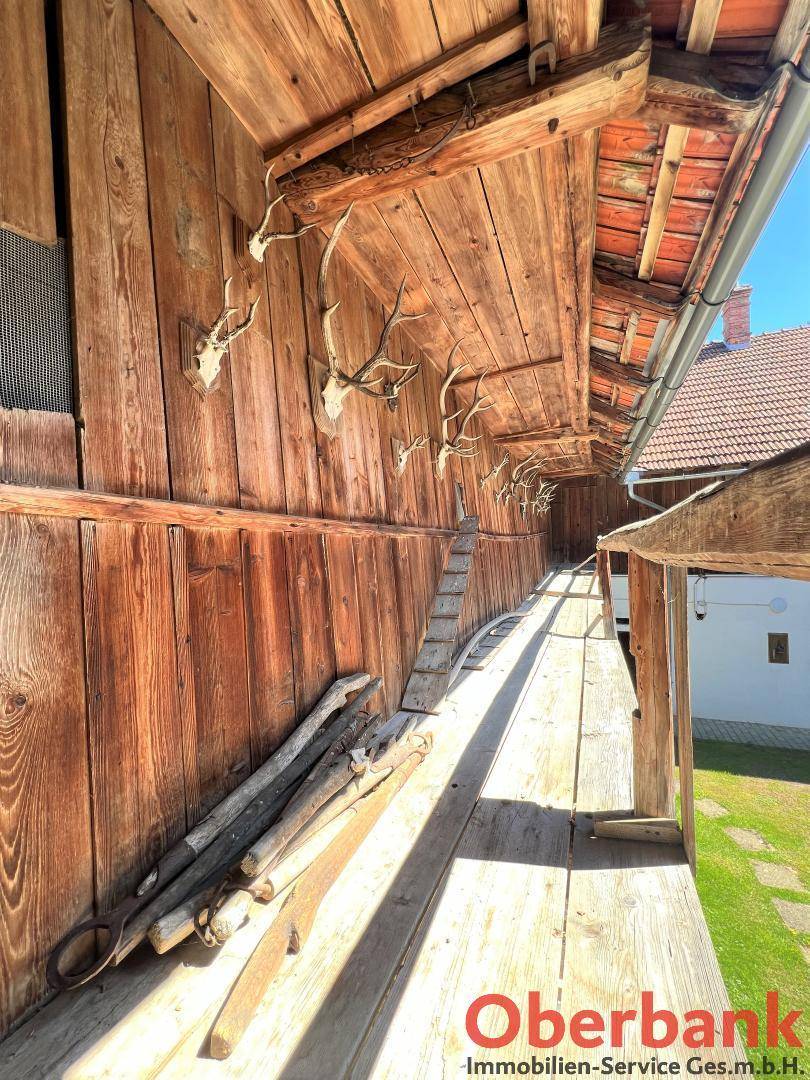 Rustikaler überdachter Gang mit Holzwänden und Decke, verziert mit Hirschgeweihen, bietet Zugang zu Räumen.