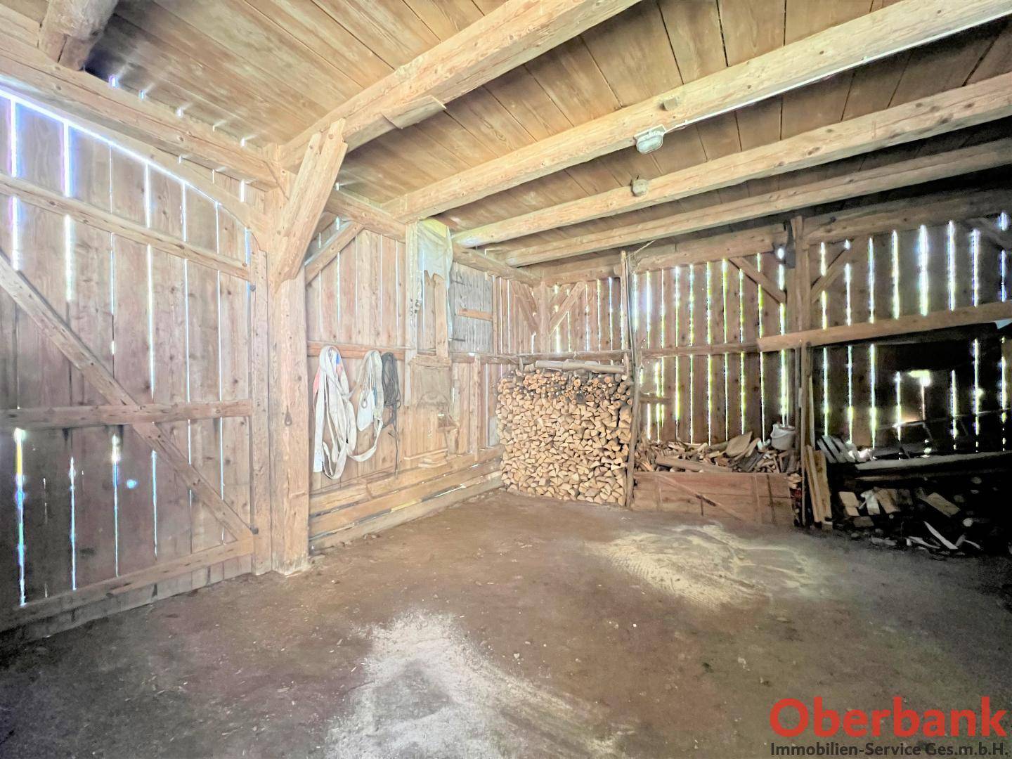 Geräumiger Lagerraum mit Holzwänden und -decke, gefüllt mit Brennholz und landwirtschaftlichen Geräten.
