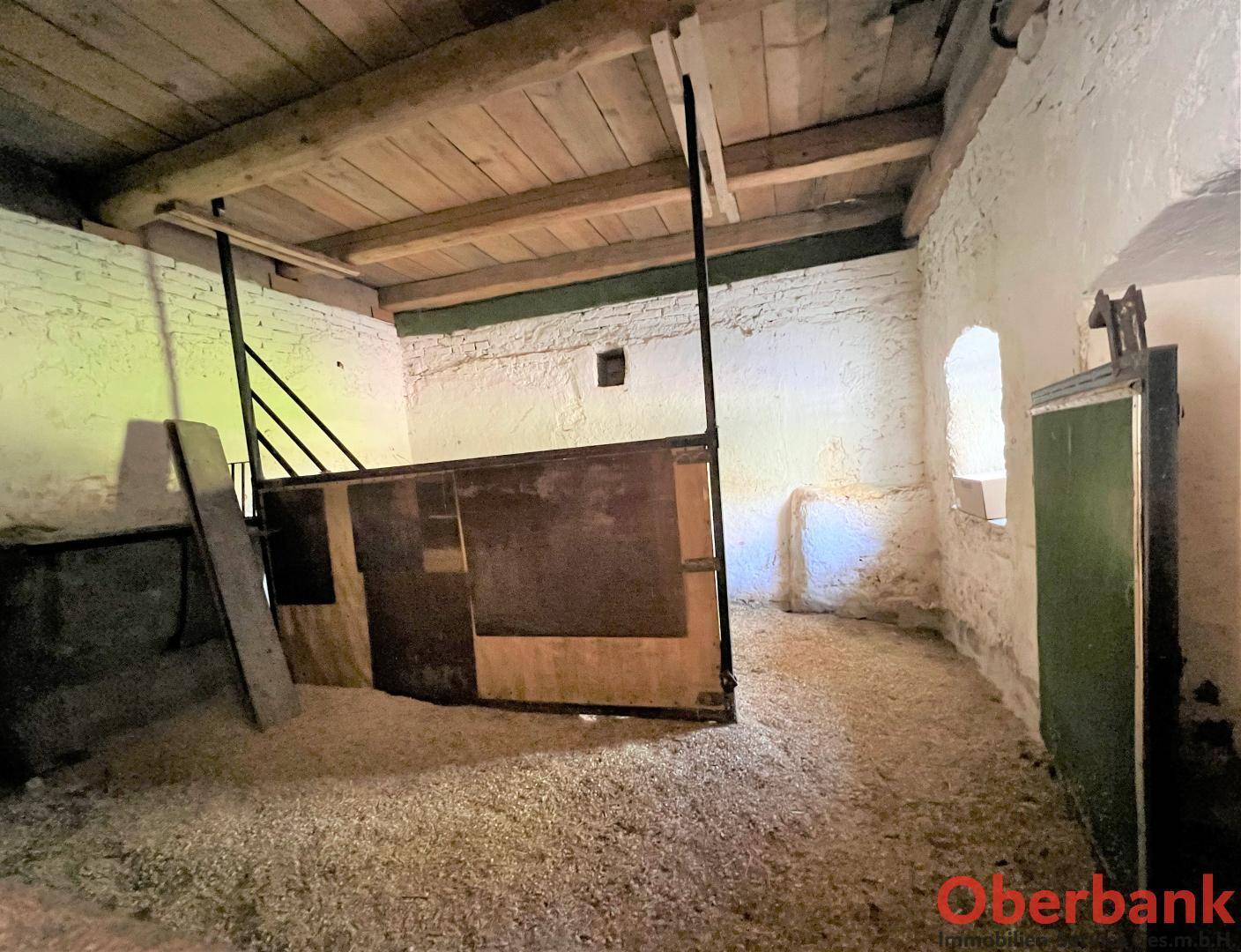 Rustikaler Stallraum mit sichtbaren Holzbalken an der Decke und Stroh auf dem Boden, bereit für Tiere.