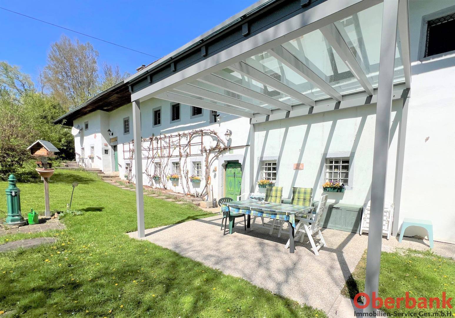 Überdachte Terrasse mit Gartenmöbeln und Blick auf den grünen Garten und das historische Bauernhaus.