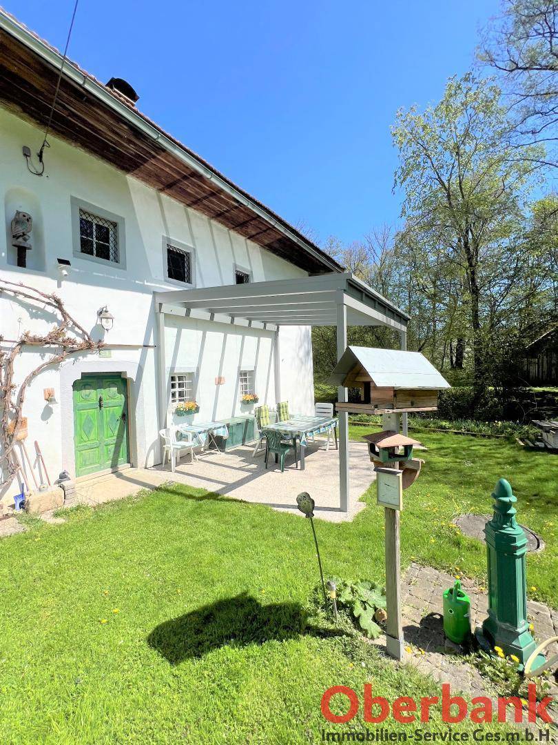 Gemütliche überdachte Terrasse mit Sitzgelegenheiten, umgeben von einem gepflegten Rasen und blühenden Pflanzen.