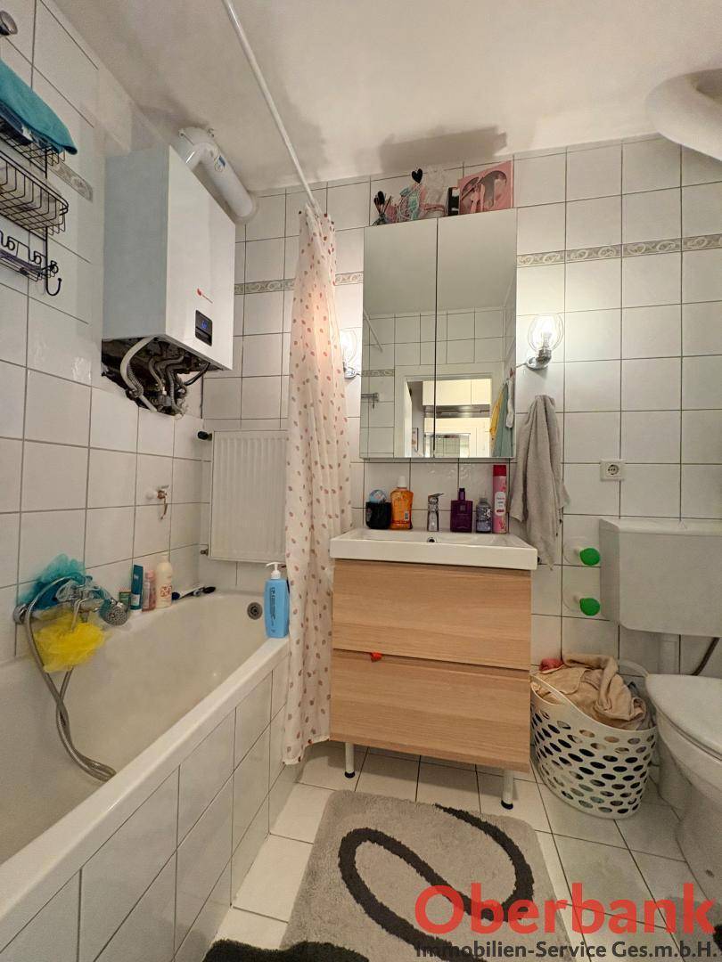 Helles Badezimmer mit Badewanne, Waschbeckenunterschrank und weißen Fliesen an den Wänden.