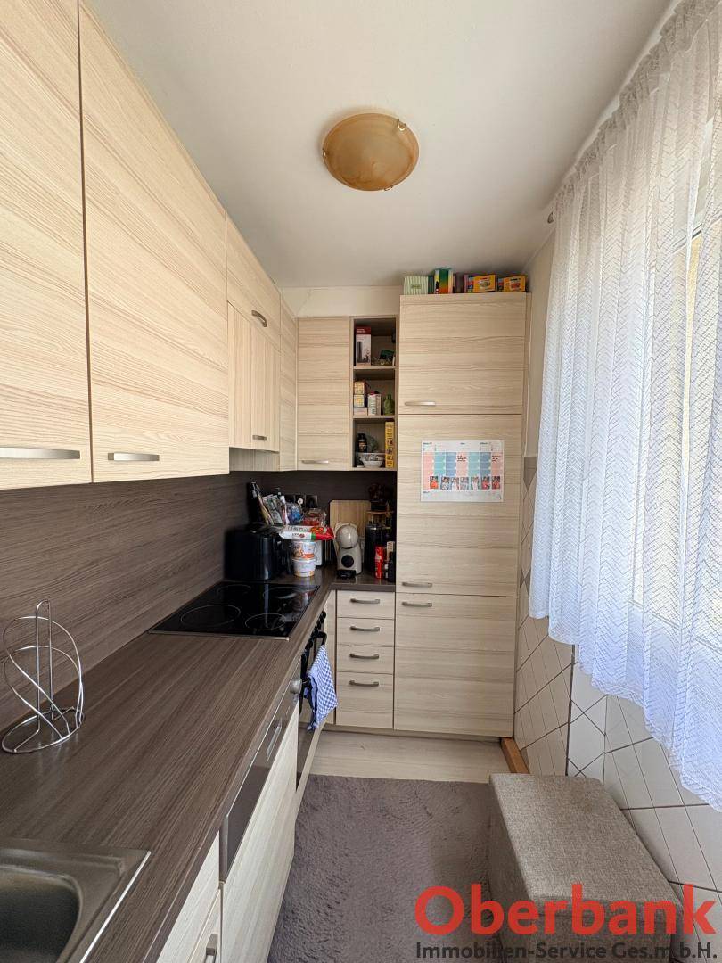 Funktionale Küche mit hellen Holzschränken, dunkler Arbeitsplatte und einem Fenster mit Vorhang.