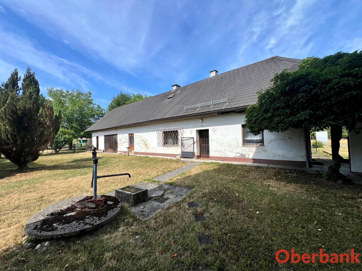 Ländliches Haus mit einem alten Wasserbrunnen im Vorgarten und trockenem Gras.