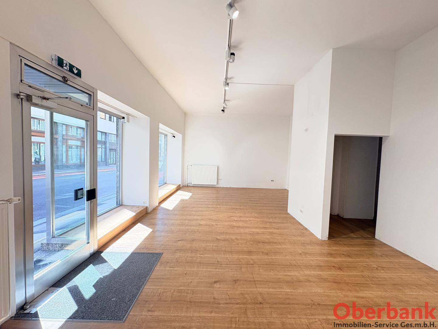 Geräumiger, heller Ladenbereich mit großen Schaufenstern und Holzboden, bereit für neue Nutzung.