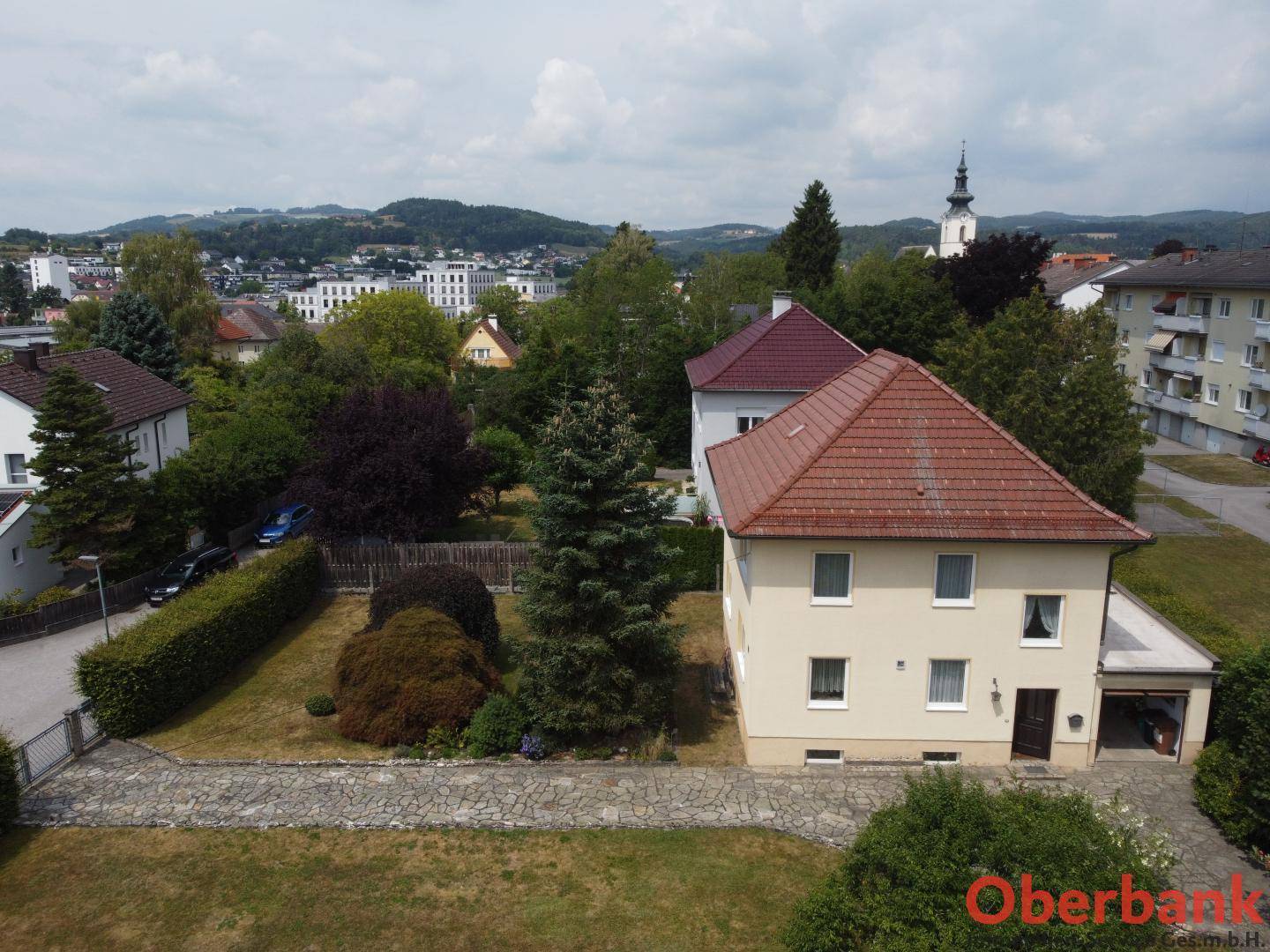 Übersicht des Einfamilienhauses mit Garten, umgeben von weiteren Gebäuden und grüner Landschaft.