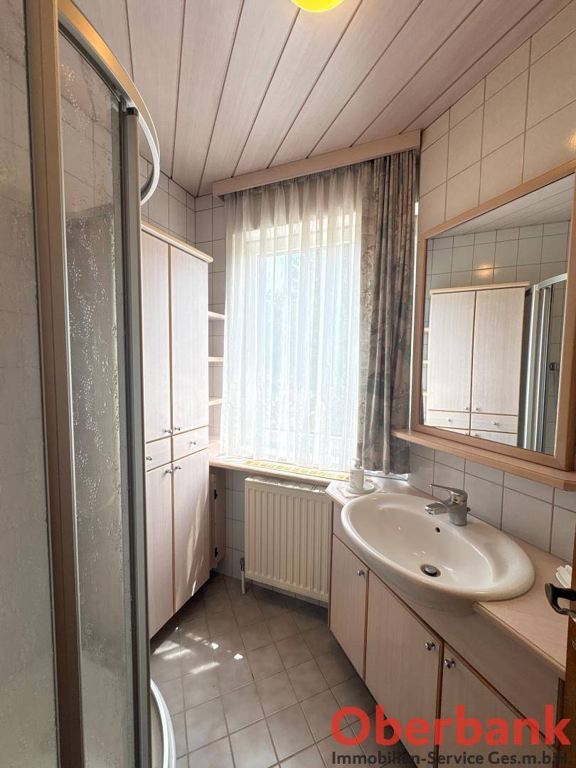 Helles Badezimmer mit Dusche, Waschbecken und Fenster, ausgestattet mit hellen Fliesen.
