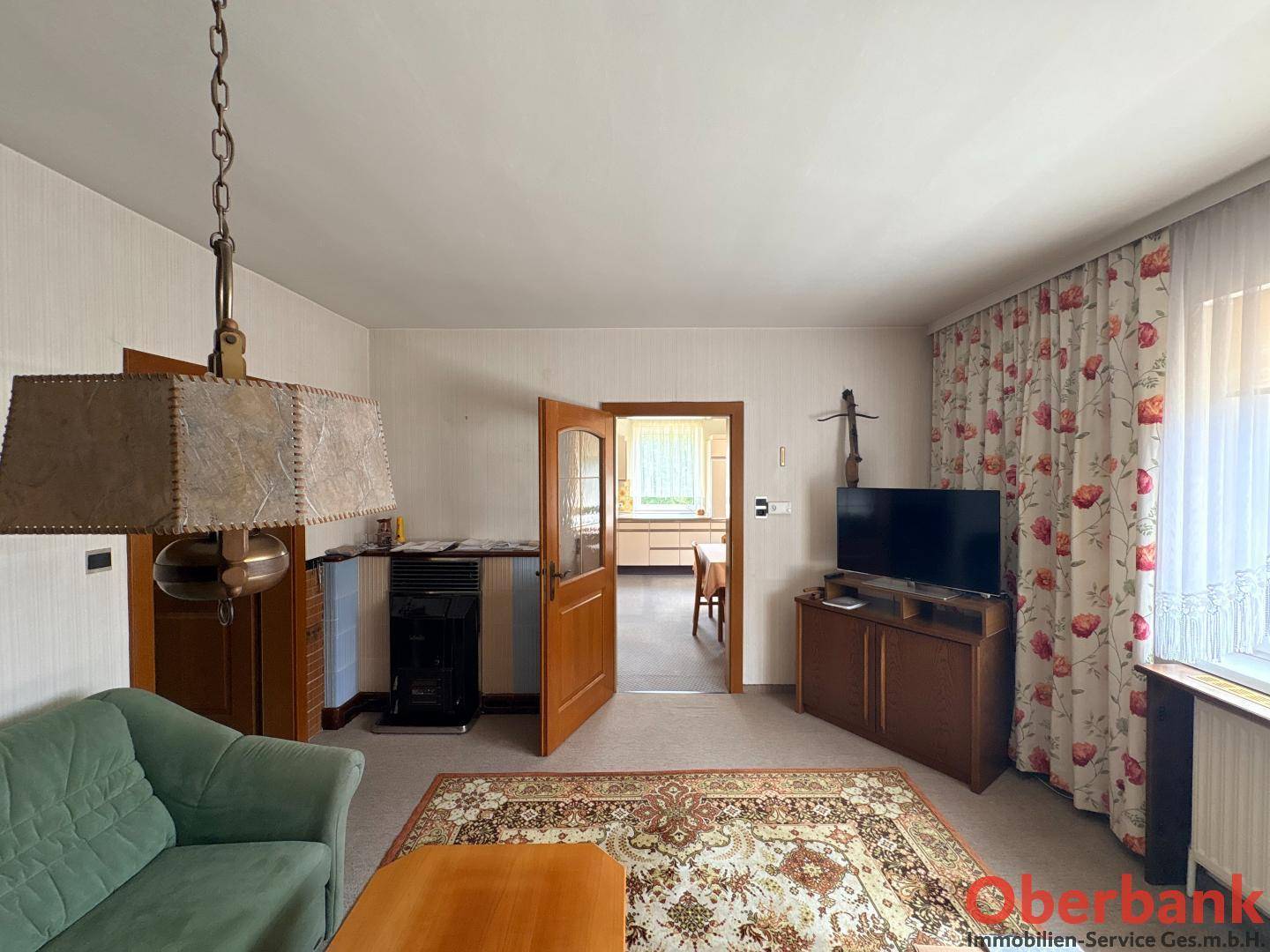 Wohnzimmer mit Sofa, Fernseher und Blick in die angrenzende Küche, ausgestattet mit Teppichboden.