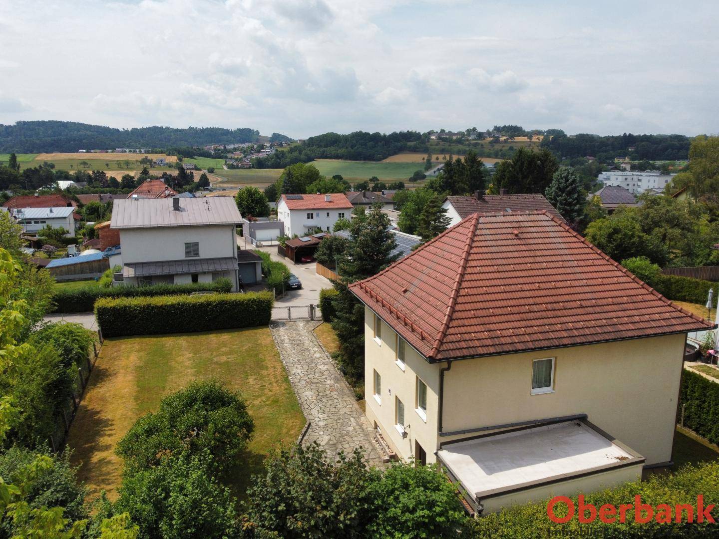 Weitläufiger Blick auf das Einfamilienhaus mit Garten und die hügelige Landschaft im Hintergrund.