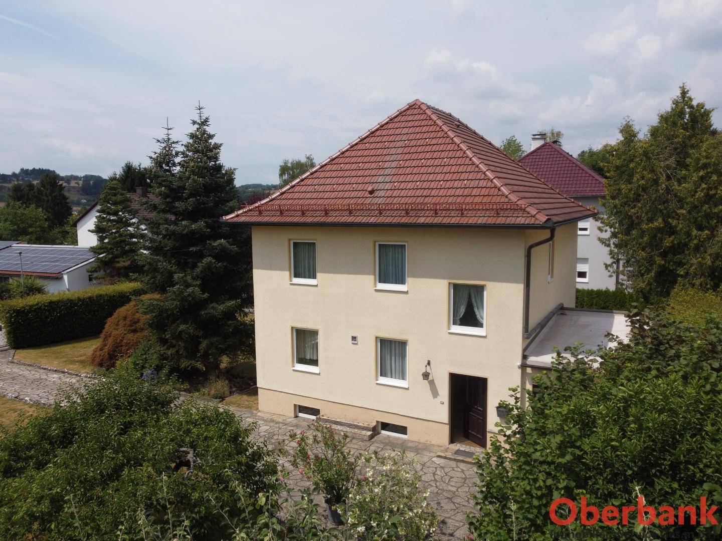 Nahaufnahme der Hausfassade mit mehreren Fenstern und dem roten Ziegeldach unter blauem Himmel.