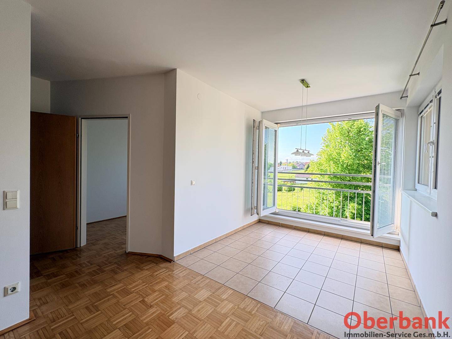Lichtdurchfluteter Wohnbereich mit Parkett- und Fliesenboden sowie Zugang zum Balkon mit Grünblick.