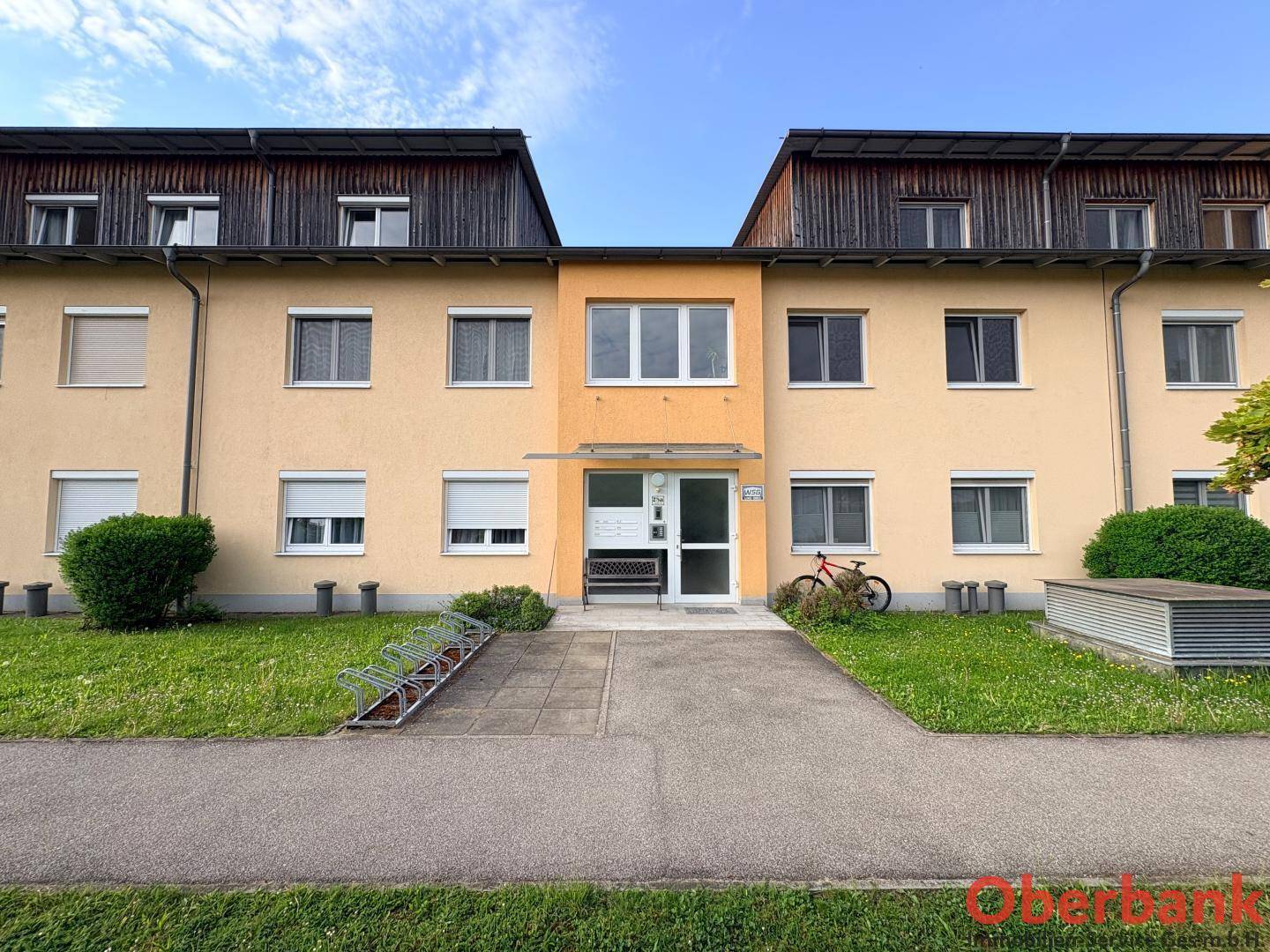 Vorderansicht des Mehrfamilienhauses mit zentralem Eingang und Fahrradständern im Vorgartenbereich.