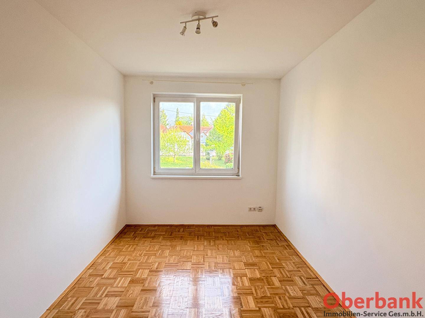 Freundliches Schlafzimmer mit Parkettboden und einem großen Fenster mit Blick auf die Umgebung.