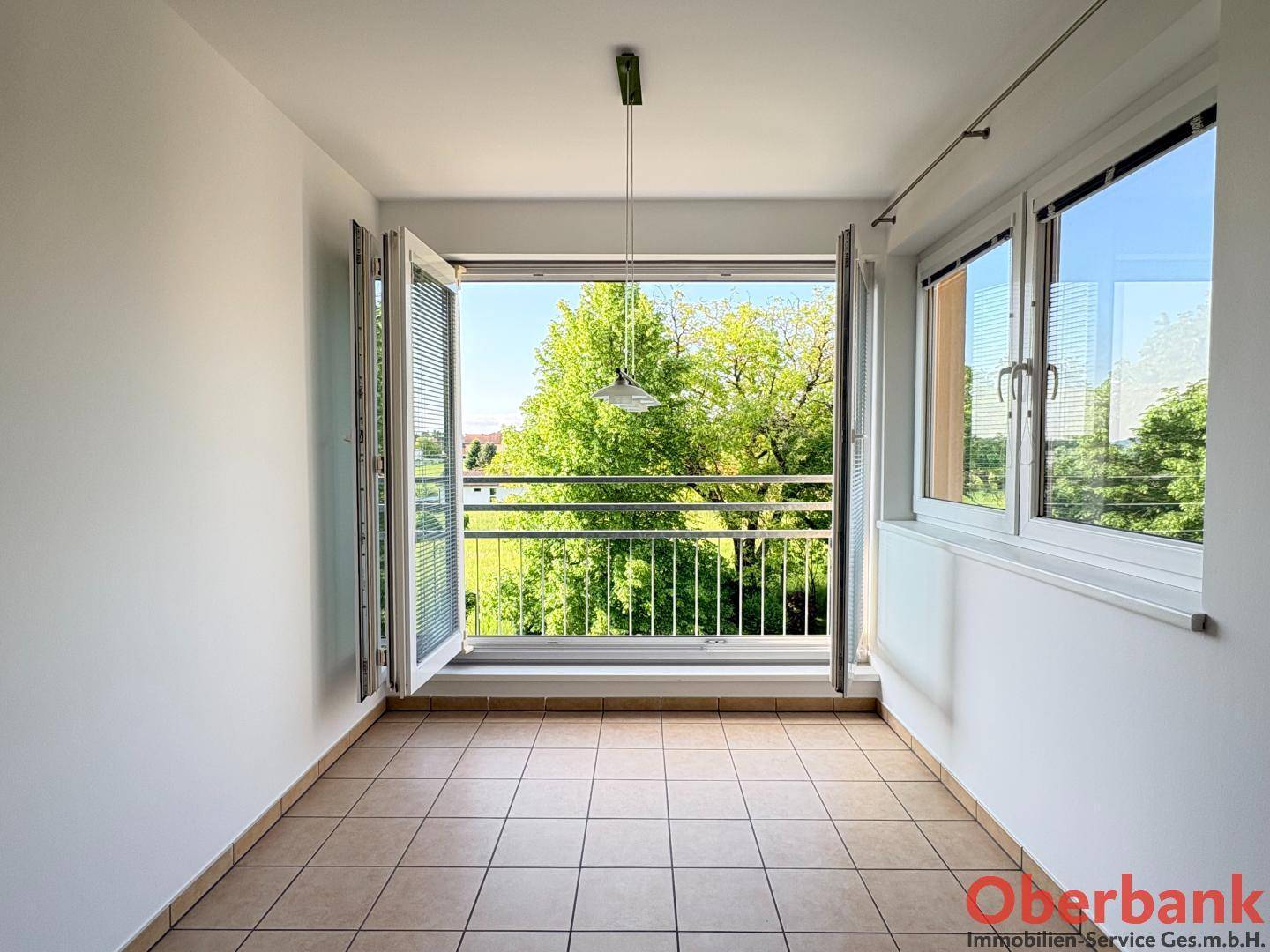 Heller Wintergarten mit Fliesenboden und weitem Ausblick ins Grüne durch geöffnete Fenster.
