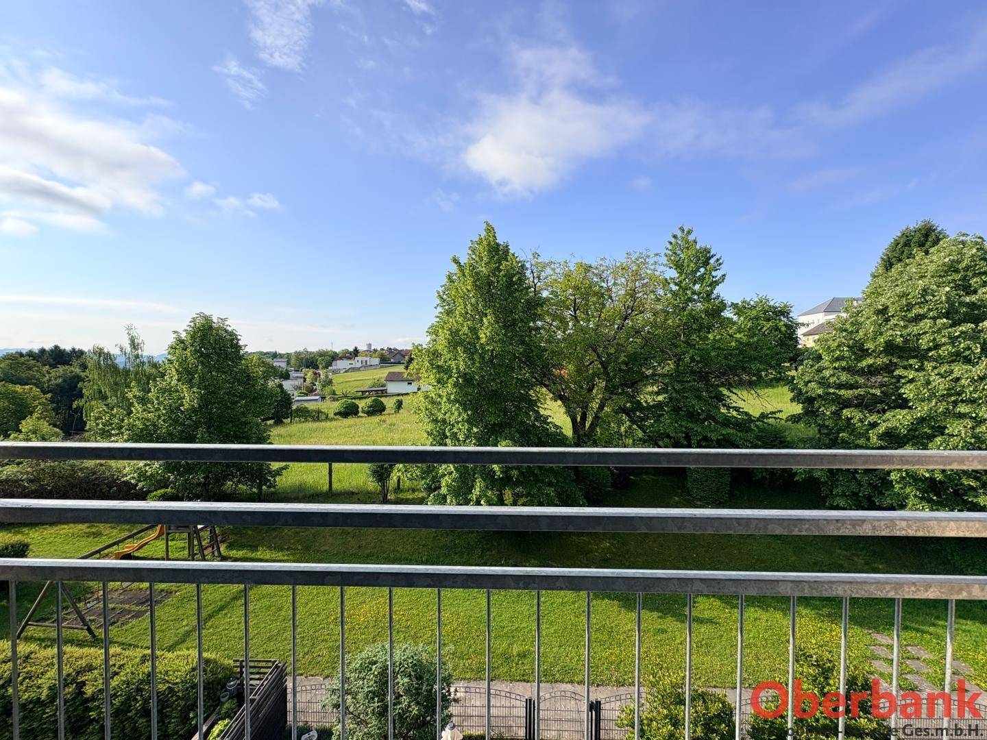 Weitläufiger Blick ins Grüne mit Bäumen und ländlicher Umgebung von einem Balkon aus.