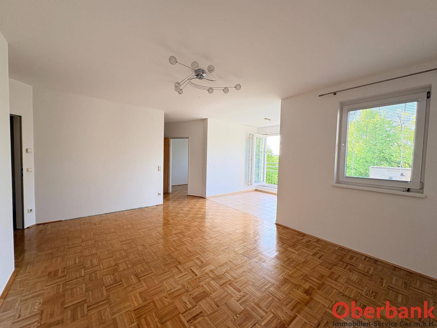 Helles Wohnzimmer mit Fischgrätparkett und einem Fenster, das viel Tageslicht hereinlässt.
