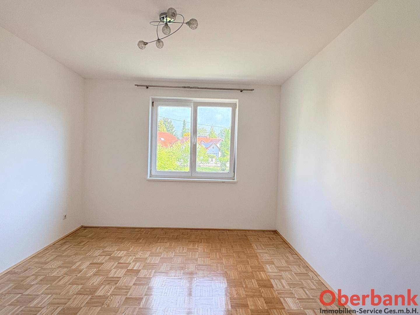 Geräumiges Schlafzimmer mit Parkettboden und einem Fenster, das viel Tageslicht hereinlässt.