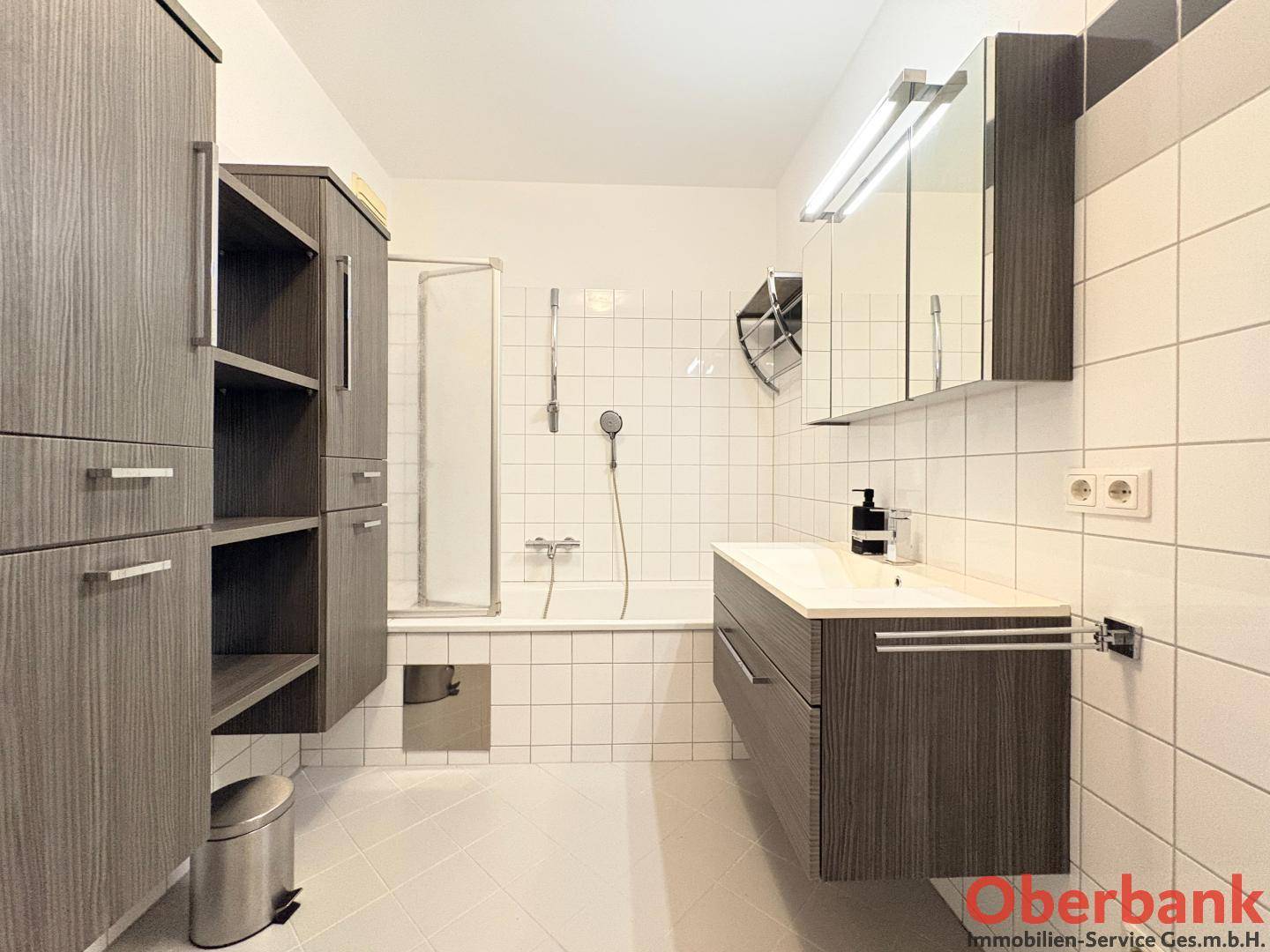 Modernes Badezimmer mit Badewanne, Duschabtrennung, Waschtisch und dunklen Holzschränken.