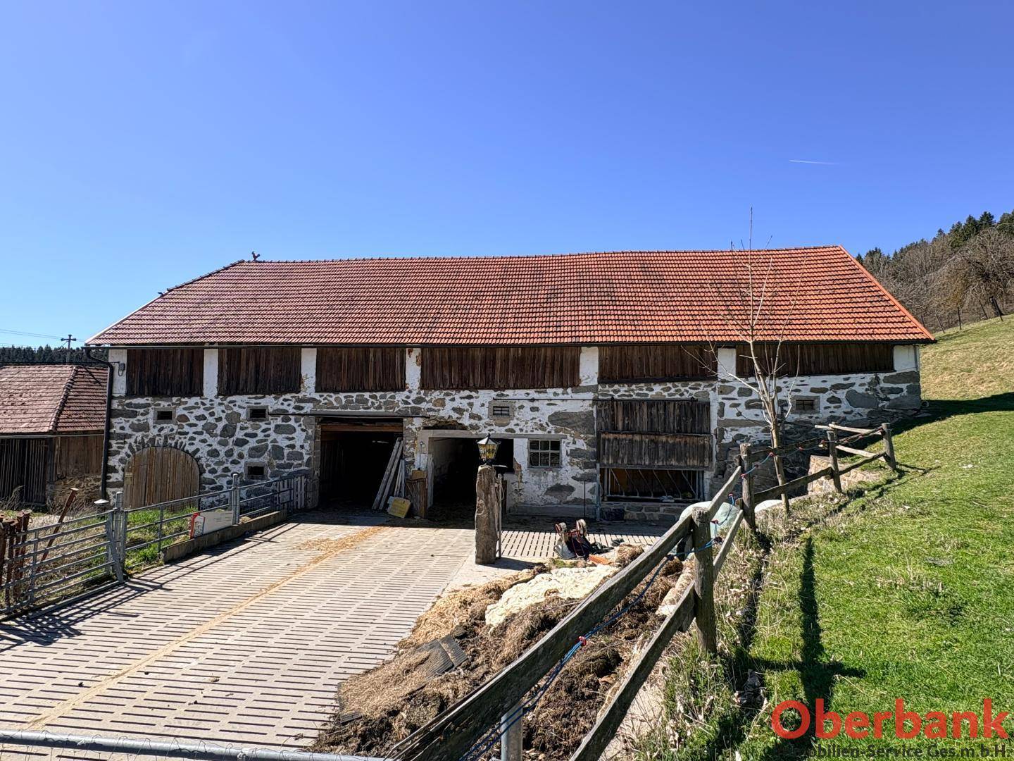 Großes Wirtschaftsgebäude mit Steinfassade und Holzelementen, umgeben von grünen Wiesen und Natur.