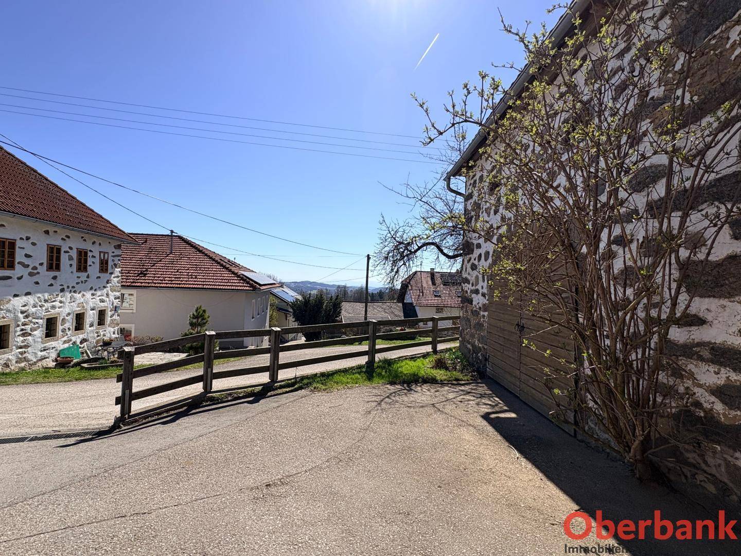 Ländliche Straße führt an historischen Gebäuden vorbei mit weitem Blick in die hügelige Landschaft.